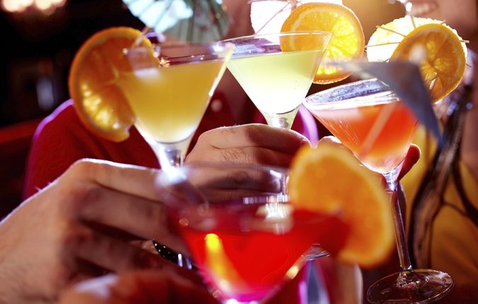 Row of martini glasses with cocktails in hands of people